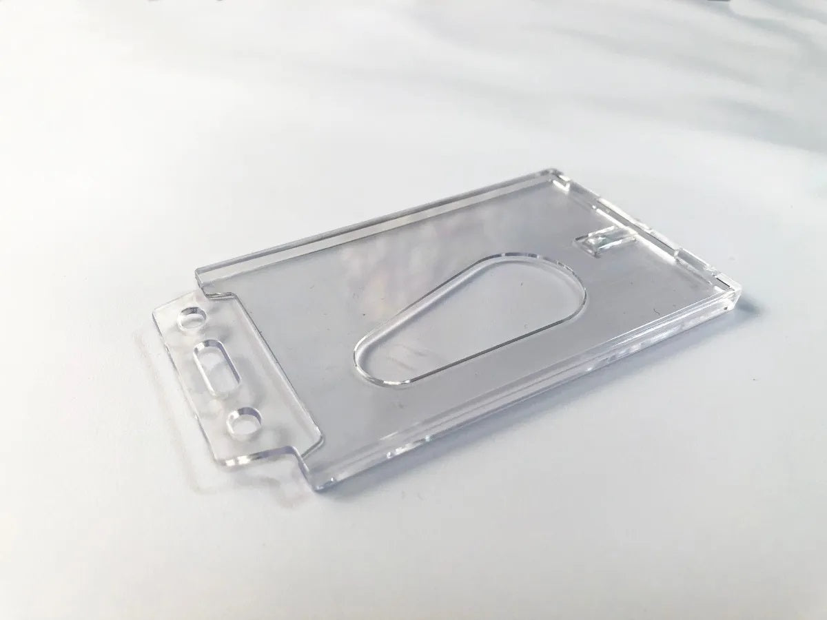 Porta gafetes en plástico rígido cristalino con orificio para gancho, yoyo, cordón o caimán. Orientación vertical, tamaño 8.5 x 5.5 cm, ideal para credenciales de identificación de personal, duradero y resistente.