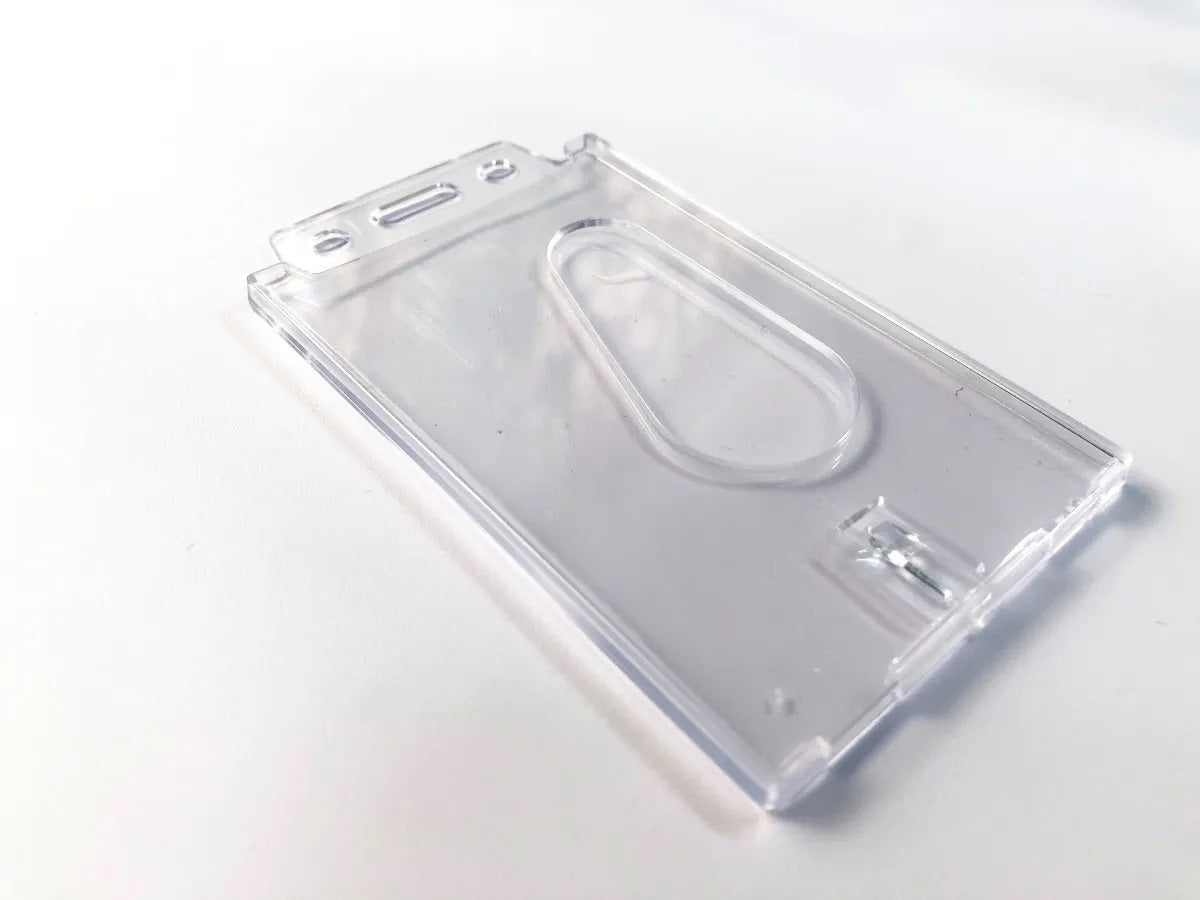 Porta gafetes en plástico rígido cristalino con orificio para gancho, yoyo, cordón o caimán. Orientación vertical, tamaño 8.5 x 5.5 cm, ideal para credenciales de identificación de personal, duradero y resistente.